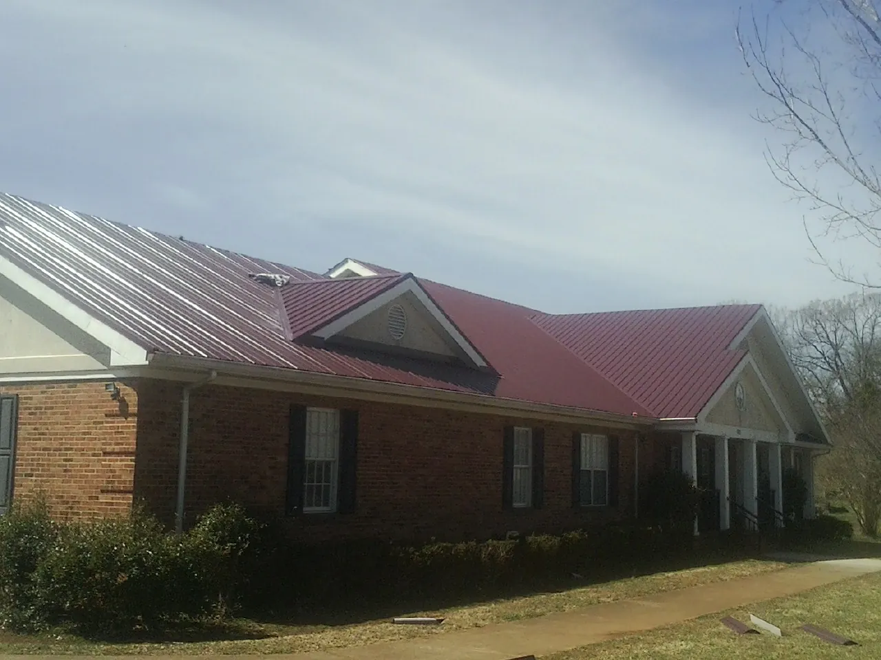 Red metal roof with gabled entries on a long brick building, from a Hail Damage Roof Repair job in Mackville