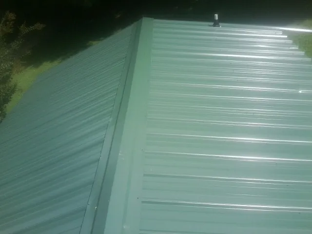 New green metal panels meeting at the ridge of a roof — Flat Roof Repair work by our crew in Mackville
