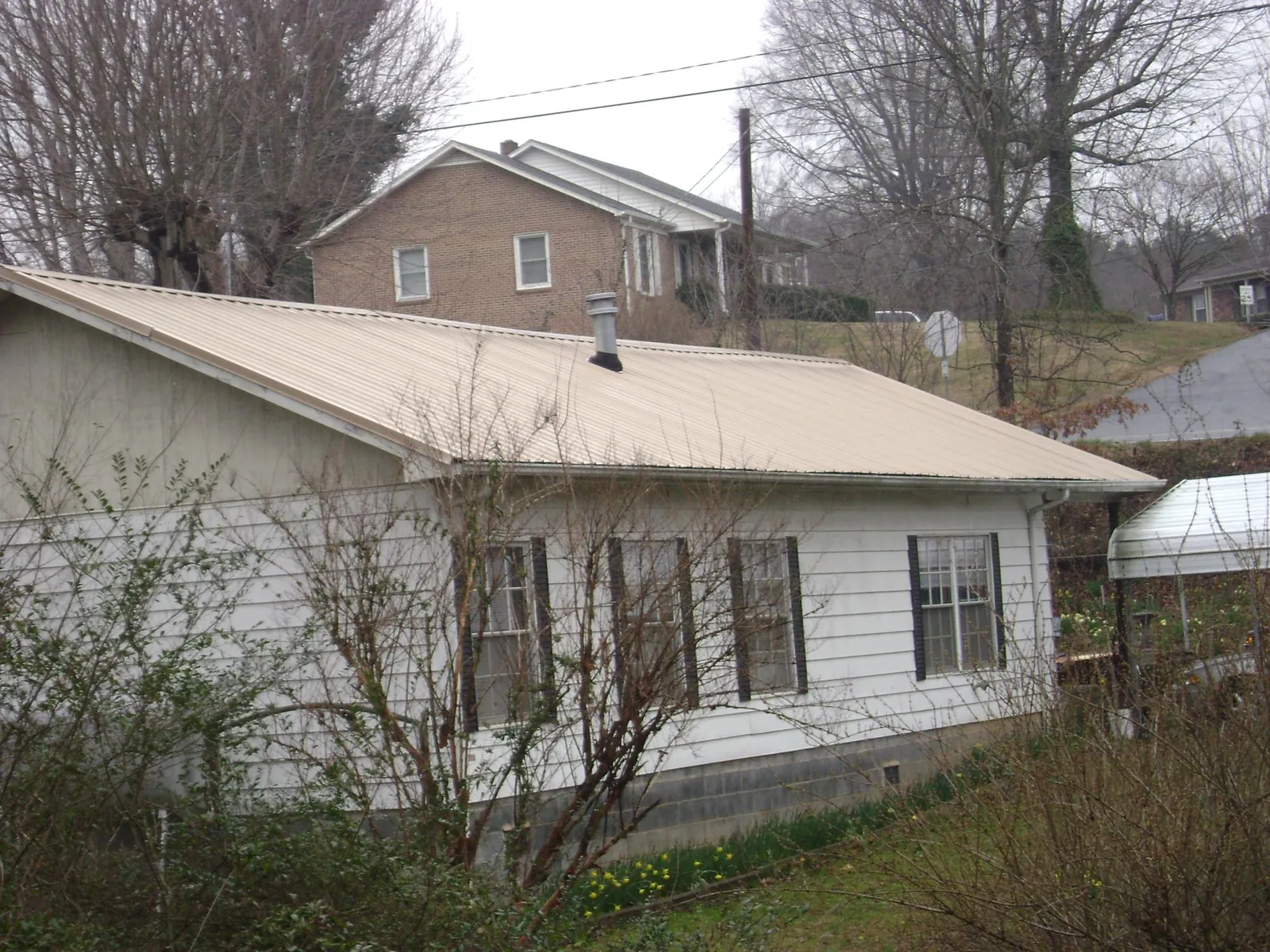 Tan metal roof on a white sided house set into a hillside — Commercial Roofing by Roofing Brothers in Mackville